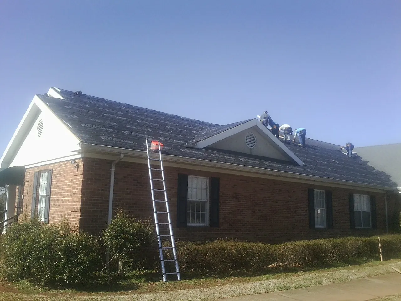 Crew tearing shingles off a brick ranch roof with a ladder set — Metal Roof Repair work by our crew in Rye
